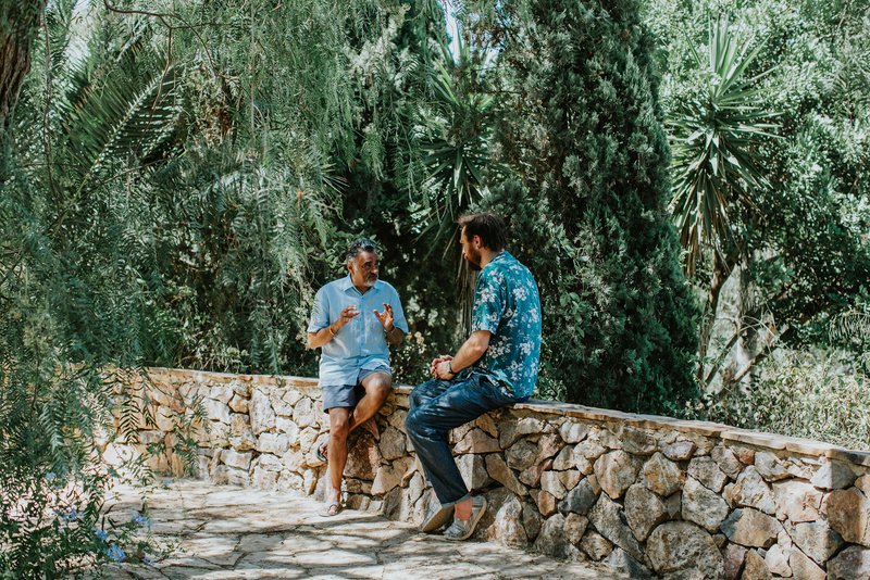 Two people talking in a garden surrounded by olive trees